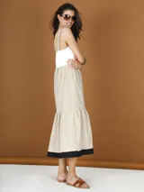 Vestido midi de popelina color beige, con breteles finos drapeados, corte imperio y falda acampanada con volado en el ruedo y detalle de borde negro.