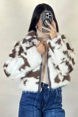 Campera corta de piel sintética con estampado de manchas tipo vaca en tonos blanco y marrón. Presenta cuello camisero, cierre frontal con cremallera y detalles en cuero sintético marrón en el cuello y la solapa del cierre.