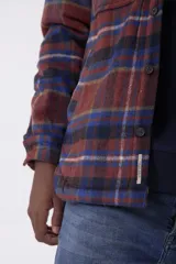 Sobrecamisa de corte holgado con diseño a cuadros en tonos beige y marrón, confeccionada en tejido de textura suave. Presenta cuello clásico, cierre frontal con botones, dos bolsillos con solapa en el pecho y puños abotonados.
