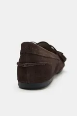 Mocasín de serraje color marrón, con detalle de fruncido en la puntera y lazo con borlas decorativas en el empeine. Presenta una suela plana de 1,5 cm.