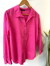 Camisa celeste de corte holgado, con cuello clásico, cierre frontal con botones, bolsillo en el pecho y mangas largas con puños abotonados.