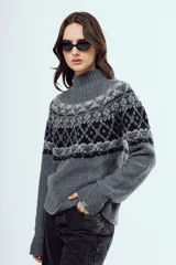 Sweater de punto color marrón, con cuello alto y diseño tejido con patrones geométricos en tonos negros y blancos en la parte superior y mangas.
