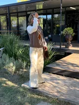 Chaleco tejido de punto en color chocolate, con cuello redondo y diseño sin mangas. Presenta un aplique frontal decorativo compuesto por tres figuras en forma de rombo en tonos tierra, bordeadas con hilo crudo.