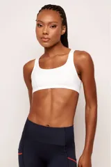 Top deportivo de alto rendimiento, color blanco, con tirantes medianos y diseño de espalda baja. Cuenta con bolsillos internos para copas removibles.