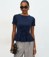 Blusa de punto roma color azul marino, con diseño estructurado, manga corta, recortes que definen la silueta, detalles de lazos decorativos en el frente y ruedo con volado peplum.