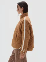 Campera acolchada color marrón claro, con cuello alto, cierre frontal y una franja vertical blanca en cada manga. Tiene bolsillos laterales y puños ajustables con botón.