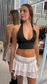 Top negro con escote halter profundo y tiras que se anudan al cuello. Presenta un detalle de apliques metalizados dorados en el tirante izquierdo y diseño corto al cuerpo.