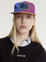 Gorro con visera colorblock, con paneles en color marrón, violeta y azul.