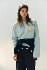 Camiseta de algodón con efecto lavado en color verde menta, de corte oversize, cuello redondo y manga larga. Presenta un pequeño estampado delantero diseñado por Agustina Shuan.