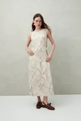 Vestido largo sin mangas con diseño cruzado y lazo lateral. Confeccionado en mezcla de lino y viscosa, presenta un estampado sutil de hojas en tonos marrones sobre un fondo beige y una abertura frontal que aporta movimiento.