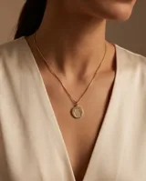 Collar de bronce dorado con cadena fina de eslabones y dije circular con la figura de una mano de Fátima (Hamsa) texturizada en el centro.