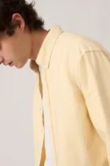 Camisa de manga larga color amarillo claro con cierre frontal de botones, cuello camisero y calce clásico.