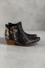 Botas de caña corta de cuero negro jaspeado, pintadas a mano con arte en tonos dorados, plateados y marrones en la parte trasera. Cuentan con doble cierre lateral con tiradores metálicos personalizados, puntera fina y taco cuadrado de madera.
