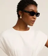 Blusa blanca de algodón con cuello redondo y mangas cortas. Presenta pliegues delanteros y traseros con efecto corsetado.