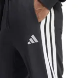 Pantalón de jogging Adidas modelo M 3s Ft Tc Pt, color negro con las tres tiras características en los laterales de color blanco y el logo de la marca bordado en la pierna izquierda. Cuenta con cintura elástica con cordón de ajuste y puños en los tobillos.