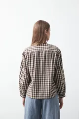 Camisa de algodón con estampado de cuadros vichy en tonos azul y blanco. Presenta escote en V con cierre frontal de botones, mangas largas con puños y un corte levemente holgado con frunces en hombros y espalda.