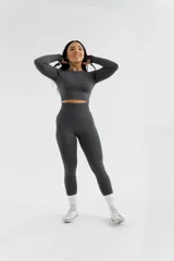 Remera deportiva de manga larga, confeccionada en tejido técnico elástico de color gris oscuro, con diseño ajustado al cuerpo y cuello redondo.