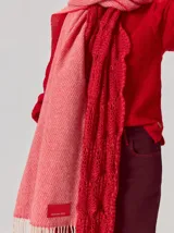 Bufanda de gran tamaño en color mostaza con diseño de tejido en espiga y flecos en los extremos. Incluye una etiqueta metálica decorativa en una de las esquinas.