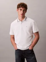 Chomba de piqué blanca Calvin Klein, de corte regular y manga corta, con cuello clásico con líneas grises en contraste y cartera de dos botones. Cuenta con el monograma CK bordado discretamente en el pecho.