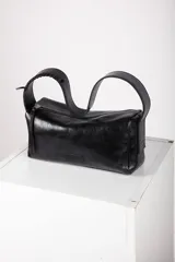 Cartera tipo baguette confeccionada en cuero de color marrón oscuro, con diseño alargado, cierre diagonal y correa de hombro.