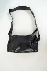 Cartera de hombro color negro con acabado brillante, diseño rectangular y correa ajustable con detalles metálicos.
