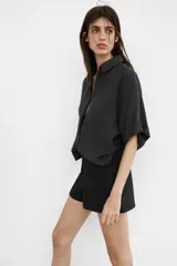 Camisa de corte fluido confeccionada en mezcla de modal, con cuello solapa, manga corta con dobladillo y bolsillo de plastrón en el delantero. Presenta cierre frontal con botones ocultos por tapeta y aberturas laterales en el bajo.