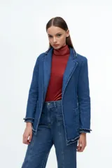 Blazer de denim azul con solapas y puños decorados con volados desflecados. Presenta un corte estructurado con bolsillos laterales y cierre frontal.