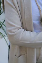 Saco abierto tipo cárdigan color crudo, de corte recto y largo medio, con mangas largas y dos bolsillos frontales aplicados.