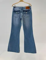 Pantalón jean de corte flare, color celeste con efecto desgastado, tiro medio y bolsillos traseros con solapa y botón.