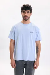 Remera celeste de manga corta, con calce relajado y pequeño estampado tipográfico en el pecho con el texto 'Arrival Coastal Club 1997'.