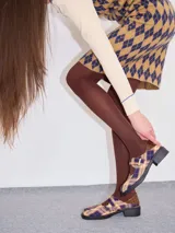 Zapatos tipo guillermina con punta cuadrada, confeccionados en lona resistente con estampado de cuadros escoceses en tonos beige, rojo y negro. Presentan una correa ajustable con hebilla metálica color bronce y una suela con taco de 4 cm.