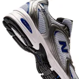 Championes urbanos New Balance modelo 530, con diseño retro de malla blanca y superposiciones en color plata y detalles en azul. Cuenta con entresuela con tecnología ABZORB para mayor amortiguación.