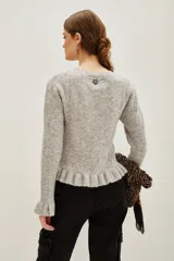 Sweater de punto color gris melange, con cuello redondo, manga larga y detalle de volado en el ruedo. Presenta pequeñas aplicaciones de strass distribuidas por toda la prenda.