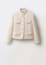 Chaqueta de tweed color crema con cuello mao, cierre frontal de botones dorados efecto joya y cuatro bolsillos delanteros con solapa. Presenta diseño recto, manga larga y forro interior.