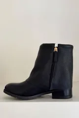 Bota de caña corta negra confeccionada en cuero, con detalle de botamanga y hebillas doradas.