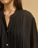 Túnica o camisa larga color blanco hueso, confeccionada en algodón, con cuello mao, frente abotonado y pliegues verticales en el pecho.
