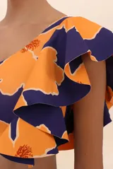 Top de bikini asimétrico con un solo hombro, estampado con flores naranjas sobre fondo azul marino y volado grande en el hombro.