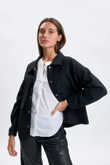 Abrigo corto de paño en color negro, con cuello camisero, cierre frontal con botones metálicos y dos bolsillos delanteros con solapa y botón.