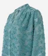 Camisa celeste en tejido chiffon con textura de bordado con felpas, cuello mao, abotonadura frontal y mangas largas abullonadas.
