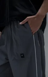 Pantalón deportivo de corte regular confeccionado en microfibra opaca, con cintura elástica y puños ajustables en los tobillos. Presenta vivos laterales a contratono que recorren toda la pierna y un pequeño parche con logo en el frente.