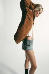 Cazadora de estilo militar confeccionada en piel de ante, con cuello subido, cierre frontal oculto con cremallera y botones a presión, bolsillos de plastrón con solapa en el pecho y bajo elástico.