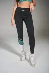 Calza deportiva larga negra con recortes en blanco y verde en la parte inferior de una pierna.