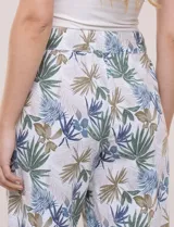 Pantalón crop de lino y rayón, con diseño wide leg de corte holgado, estampado tropical de hojas en tonos verde, azul y marrón sobre fondo blanco. Cuenta con pretina trasera elastizada y bolsillos delanteros.