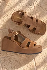 Sandalias de gamuza color marrón tostado, con plataforma corrida, tiras anchas entrecruzadas y tira ajustable con hebilla en el tobillo.