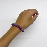 Pulsera compuesta por cuentas esféricas de piedra amatista natural de 10 mm, unidas con nudos separadores en hilo color violeta. Presenta cierre de mosquetón y detalles metálicos con baño de oro.