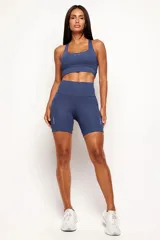 Conjunto deportivo de mujer compuesto por un top de diseño nadador y un biker de tiro alto. Ambas prendas son de color negro, confeccionadas en poliamida de alta performance con detalles reflectivos, bolsillos funcionales y recortes estratégicos para mayor comodidad y ajuste durante el entrenamiento.