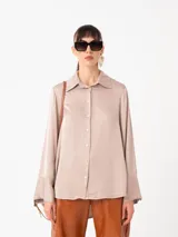 Camisa de raso color beige, con silueta suelta, manga larga, puños anchos y cierre frontal con botones a tono.