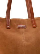 Cartera tote de gamuza color marrón maíz, con asas largas de cuero liso en tono tostado y placa con el logo de la marca en el frente.