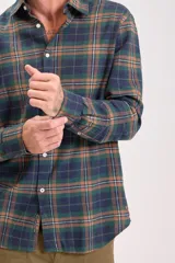 Camisa de manga larga con cuello y botones, confeccionada en tejido de franela a cuadros en tonos verde oscuro, azul marino y marrón.
