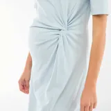 Vestido midi de color celeste, confeccionado en tejido de punto, con cuello redondo, mangas cortas y detalle de nudo o torsión en la cintura que genera un efecto drapeado, con una abertura frontal en la falda.